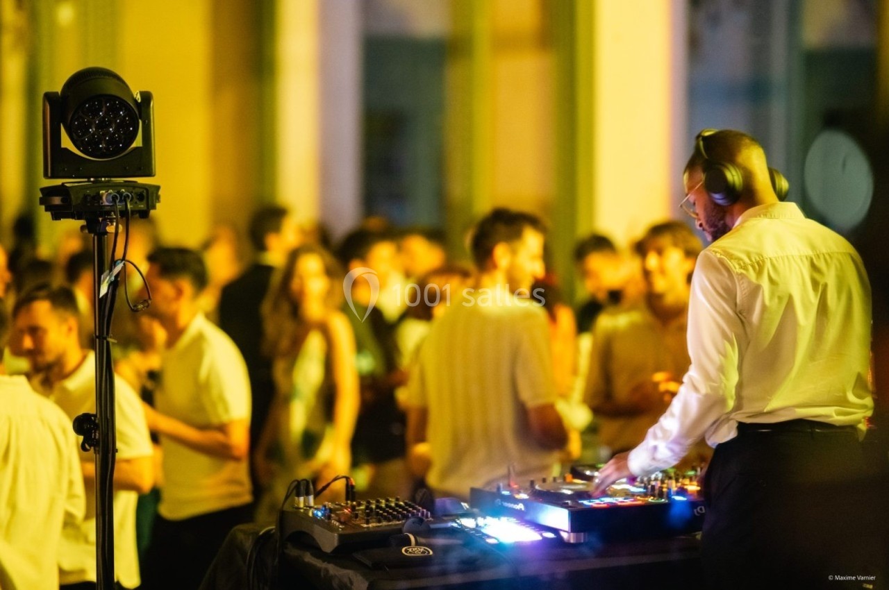 Un DJ mixe de la musique sur une table de mixage lors d'un événement en soirée avec des invités en arrière-plan.