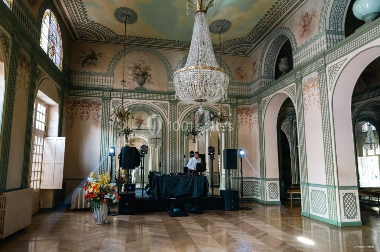 Salle élégante avec un lustre imposant, des fresques murales et un DJ installé devant une table de mixage.