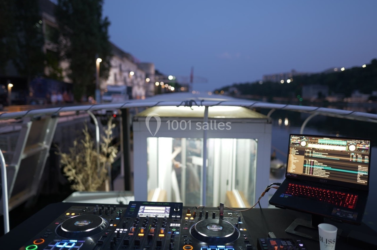 Poste de DJ avec platines et ordinateur portable sur un bateau, vue sur un canal urbain au crépuscule.