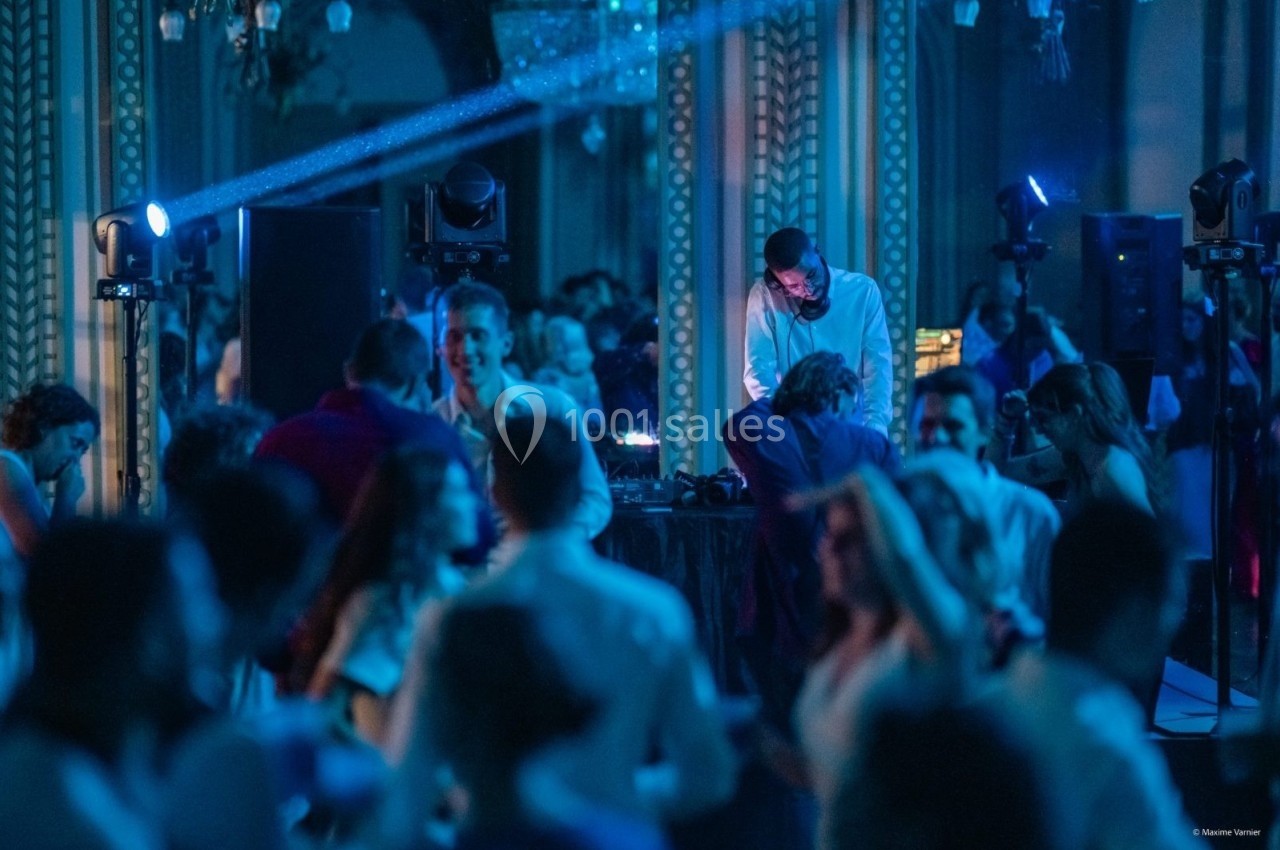 Un DJ mixe de la musique lors d'une soirée dansante, entouré de participants sous des lumières bleutées.
