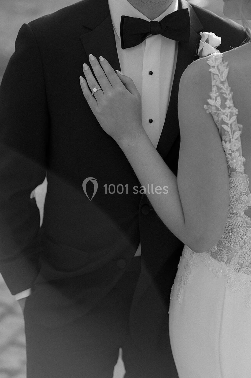 Un couple en tenue de mariage, la mariée posant sa main sur la poitrine du marié en costume noir.