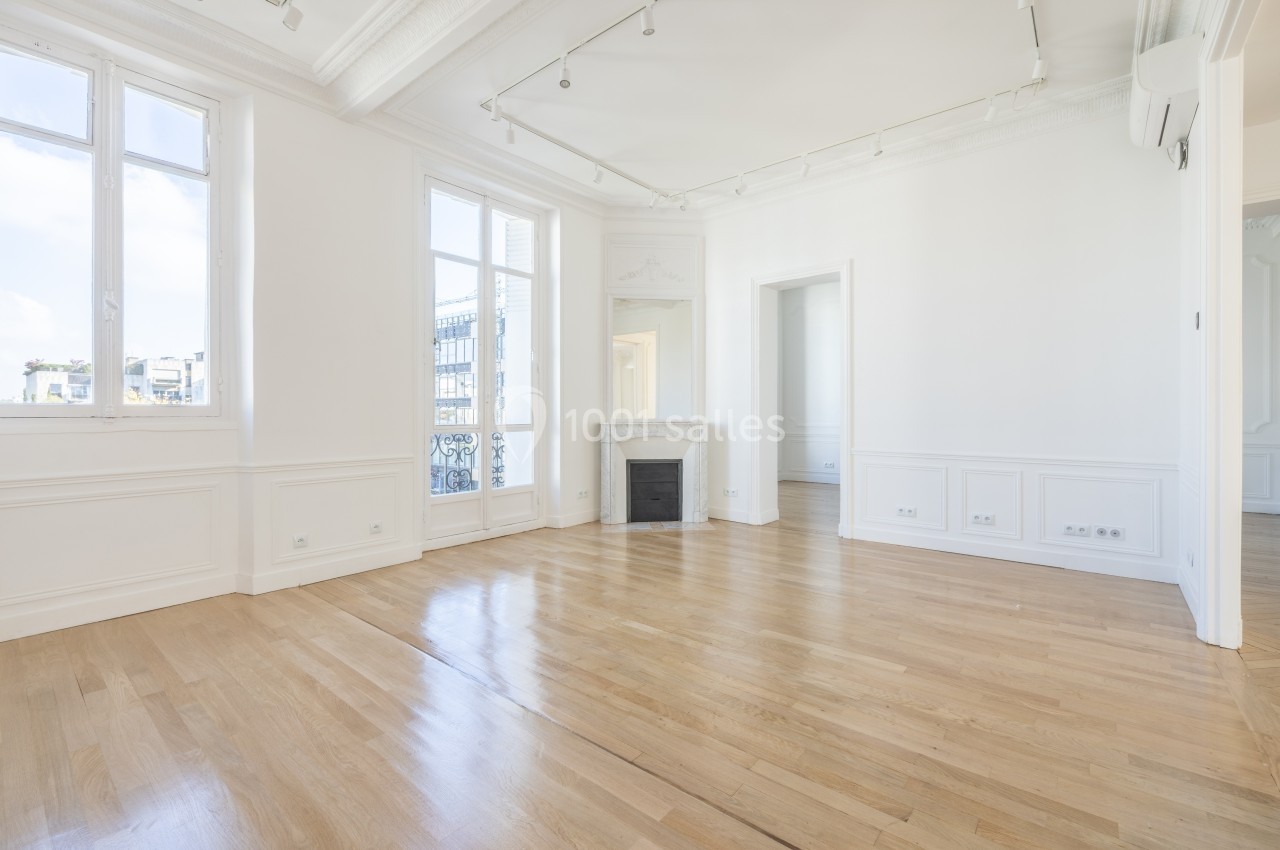 Pièce lumineuse avec parquet en bois clair, cheminée décorative blanche et grandes fenêtres donnant sur l'extérieur.
