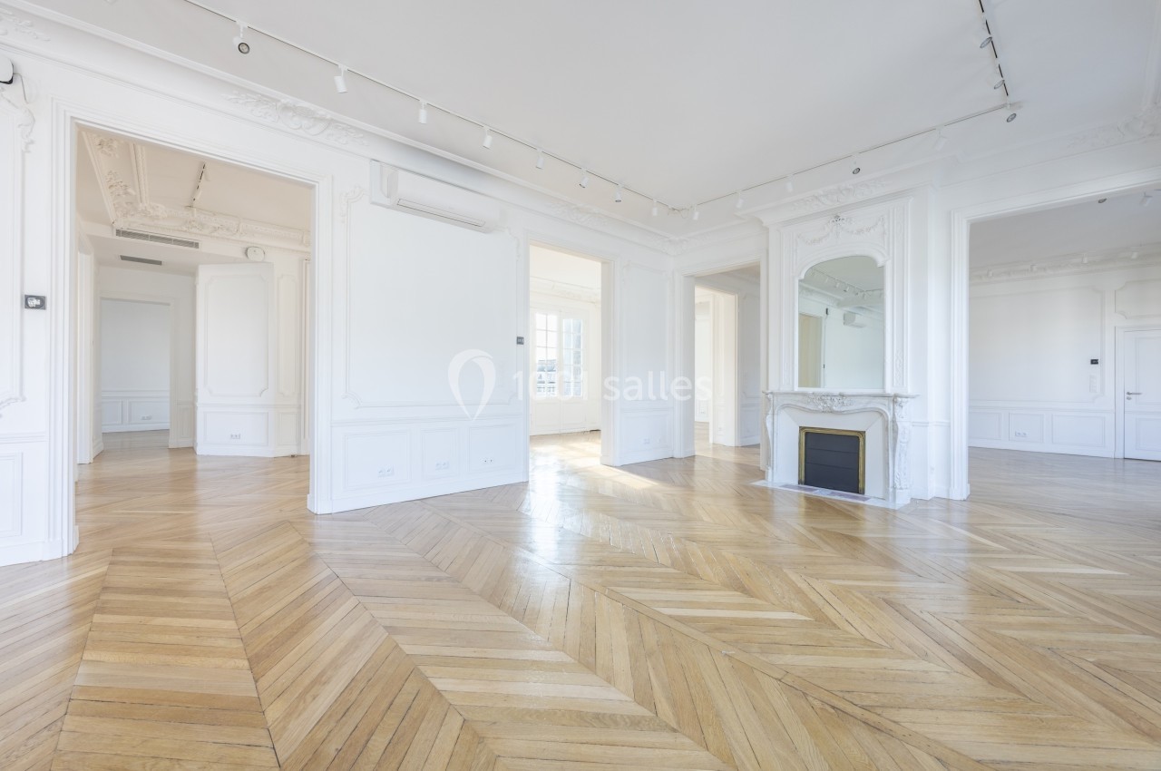 Intérieur lumineux d'un appartement vide avec parquet en chevrons, moulures blanches et cheminée avec miroir.