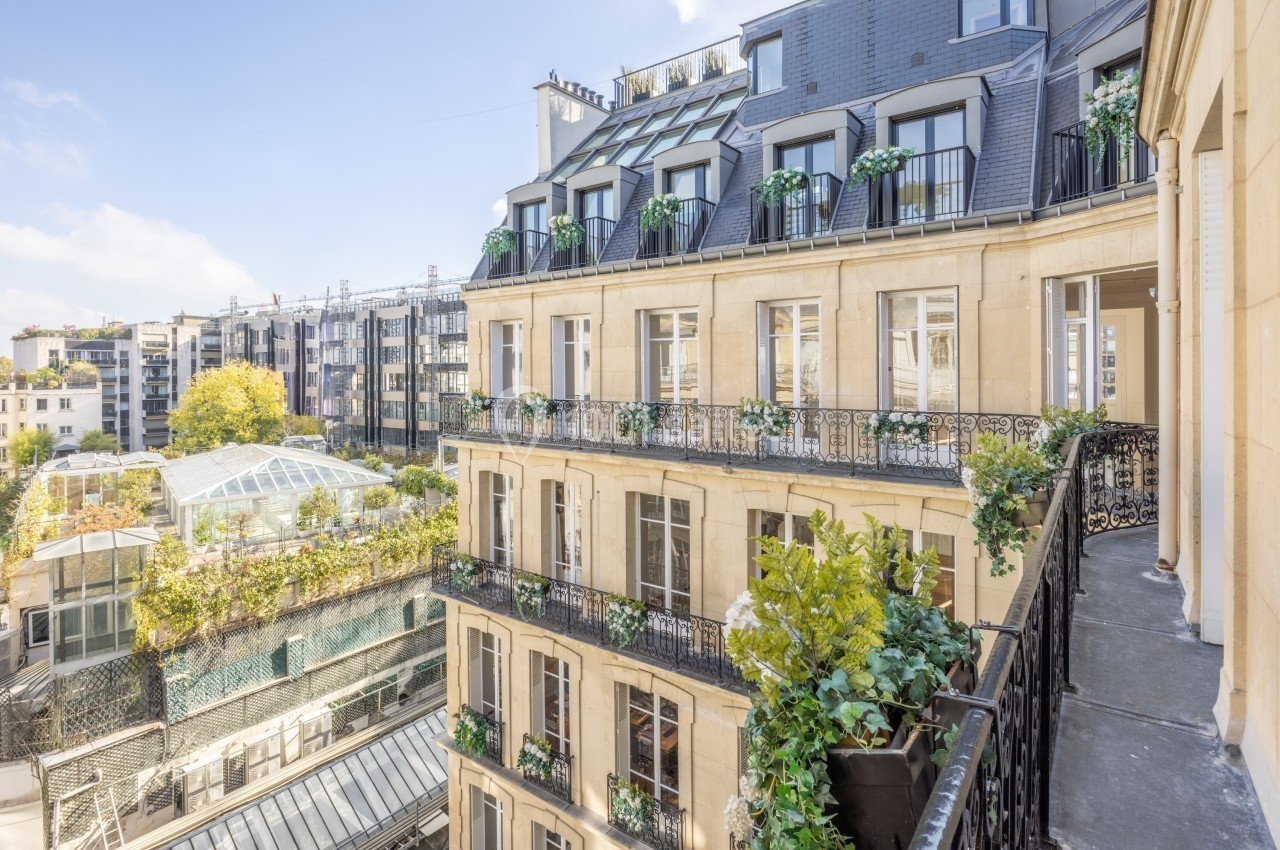 Façade d'un immeuble haussmannien avec balcons fleuris, vue sur une cour intérieure et des bâtiments modernes adjacents.