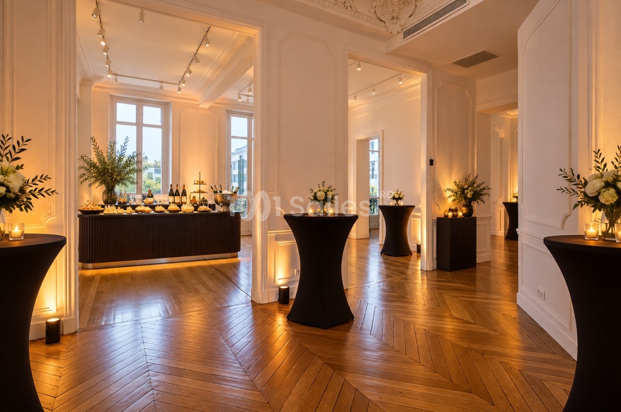 Enfilade de salons aux moulures blanches et parquet en chevrons, avec des tables hautes habillées de noir, des bouquets de fleurs et un buffet dressé au fond.