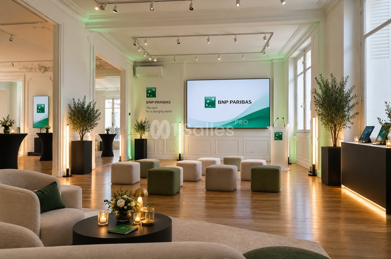 Salle haussmannienne au parquet clair, avec écran mural, rangées de poufs et pupitre devant l'écran.
