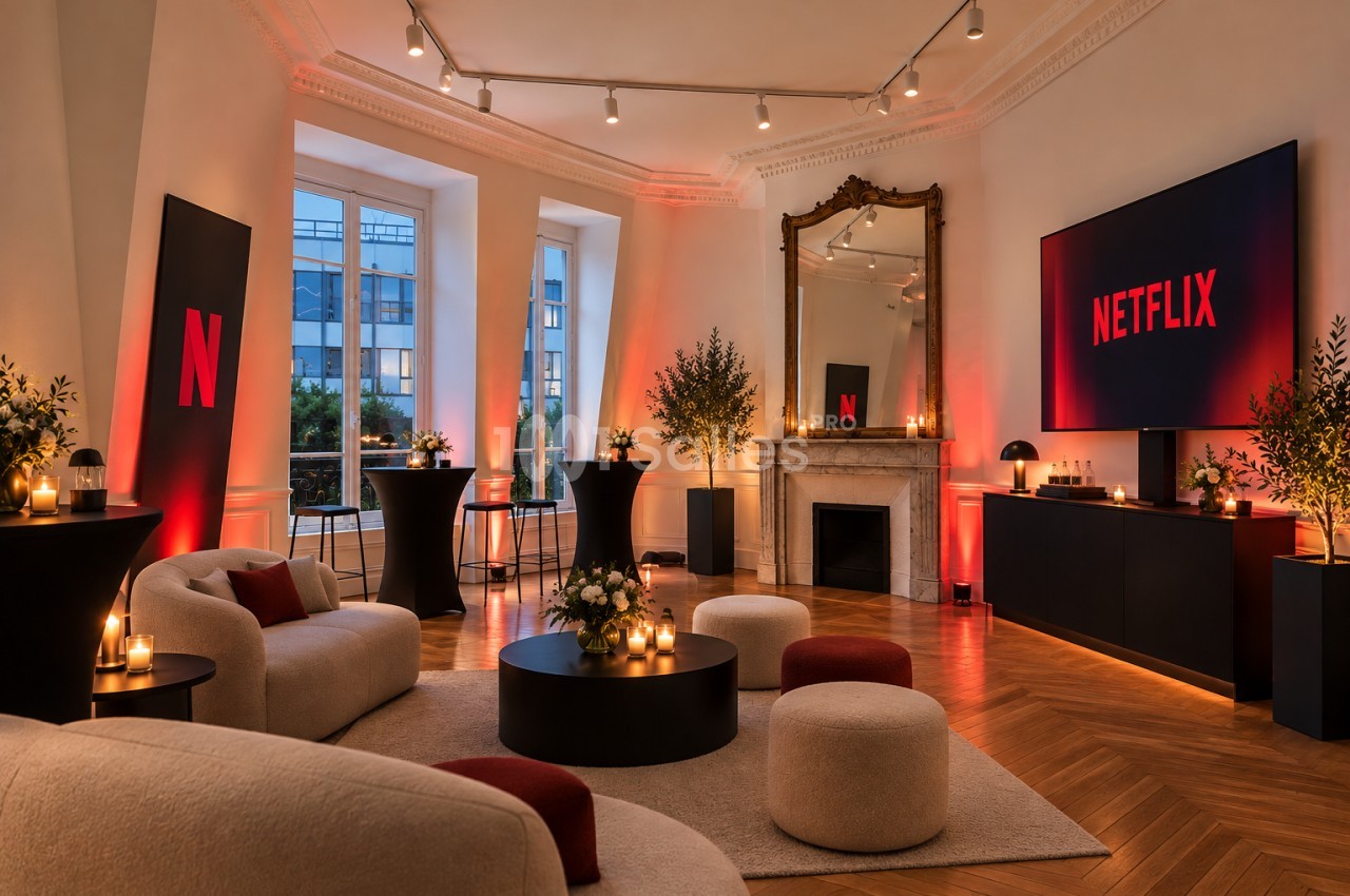 Salon haussmannien éclairé de rouge avec canapés clairs, tables hautes noires, bougies et écran sur meuble bas.