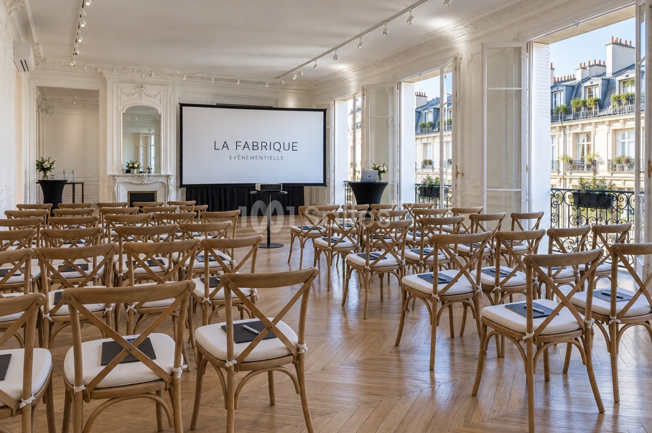 Salle de réception parisienne aux moulures blanches et parquet en chevron, dressée en conférence avec chaises en bois à dossier croisé face à un grand écran, grandes portes-fenêtres ouvertes sur un balcon. Let me check length: roughly 200 characters, too