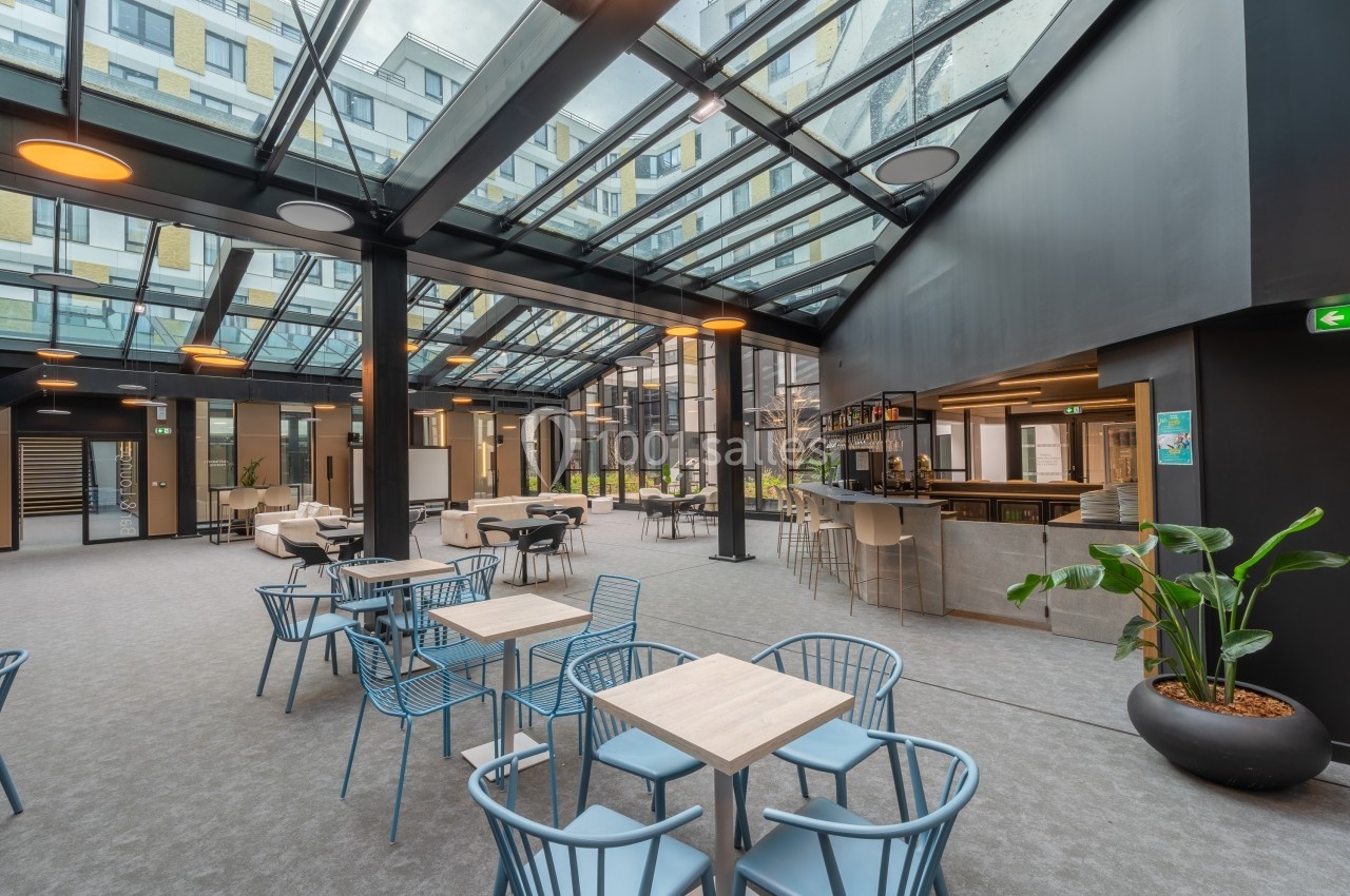 Espace intérieur lumineux avec verrière, mobilier moderne, tables, chaises et un bar dans un cadre contemporain.