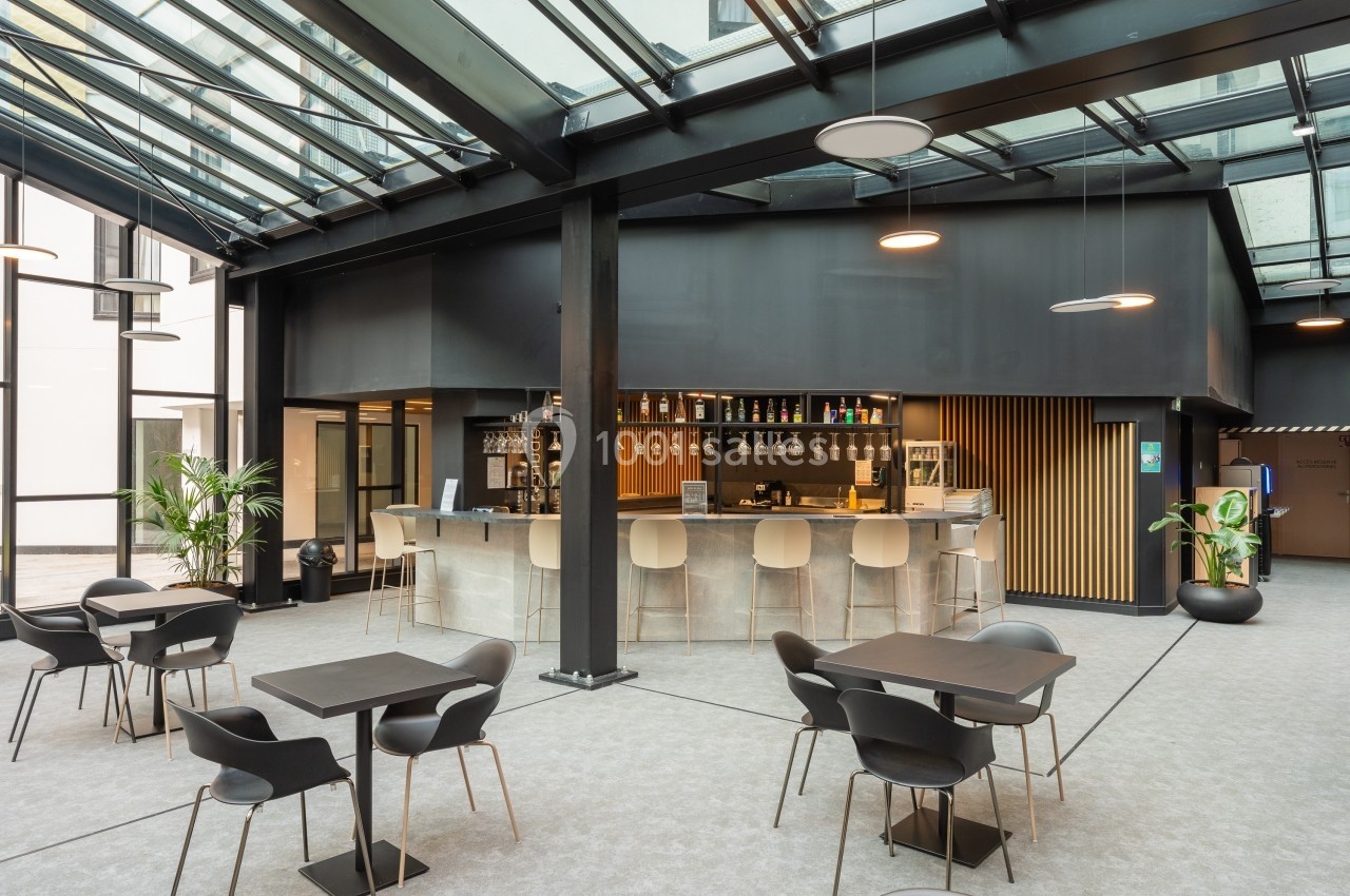 Espace intérieur moderne avec un bar central, des tables et des chaises sous une verrière.