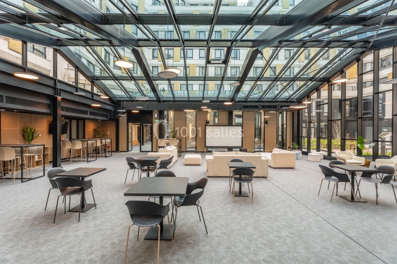 Espace intérieur lumineux avec toit en verre, mobilier moderne, tables et chaises disposées dans un cadre ouvert.
