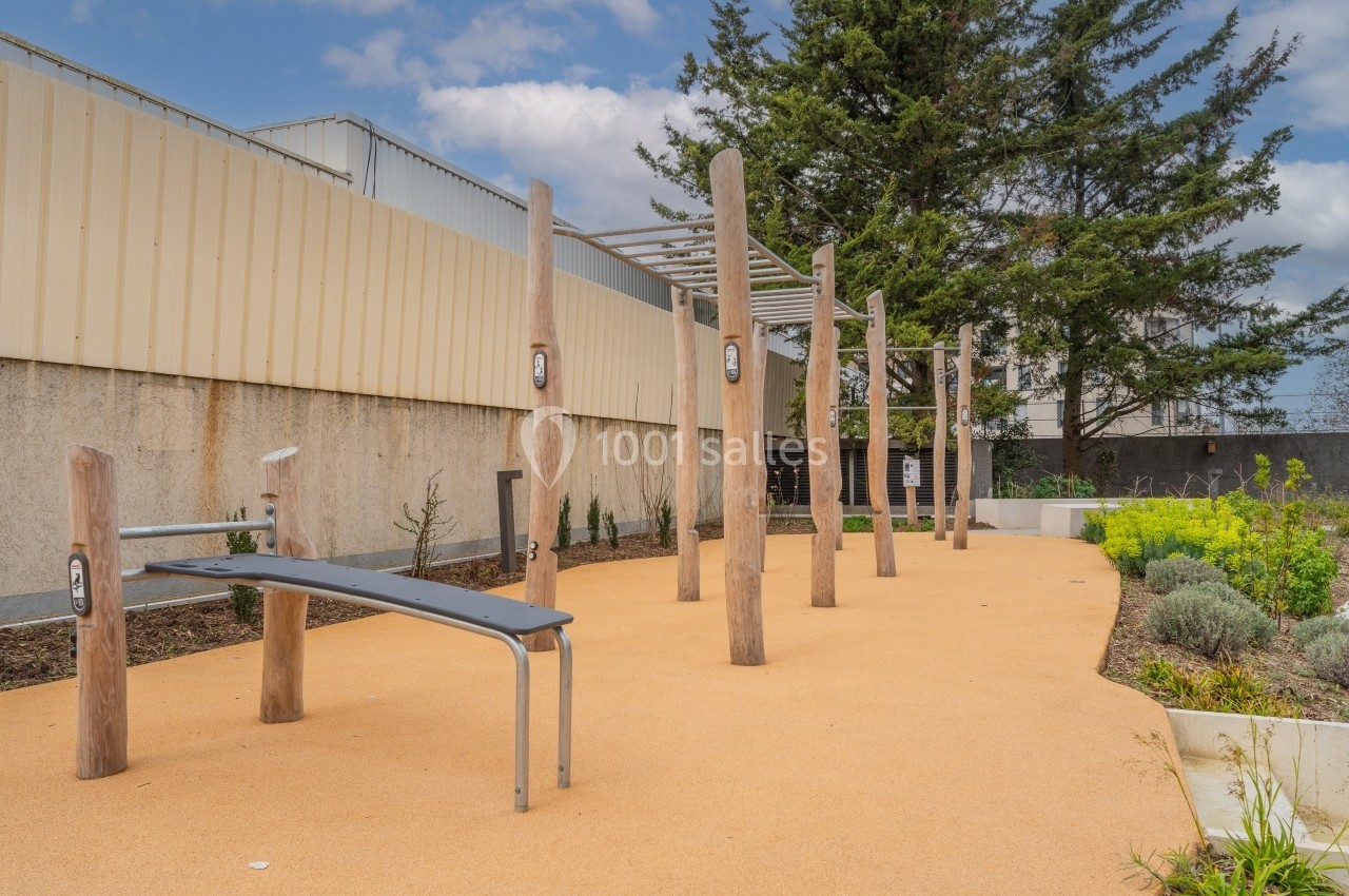 Espace extérieur avec équipements en bois pour exercices physiques, entouré de végétation et d'un sol en revêtement clair.