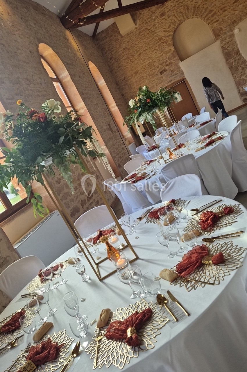 Salle de réception avec tables rondes décorées de nappes blanches, centres de table fleuris et couverts élégants.