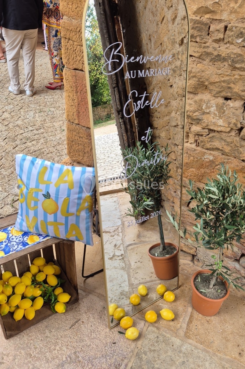 Miroir décoratif avec message de bienvenue pour un mariage, entouré de citrons, coussin et plantes.