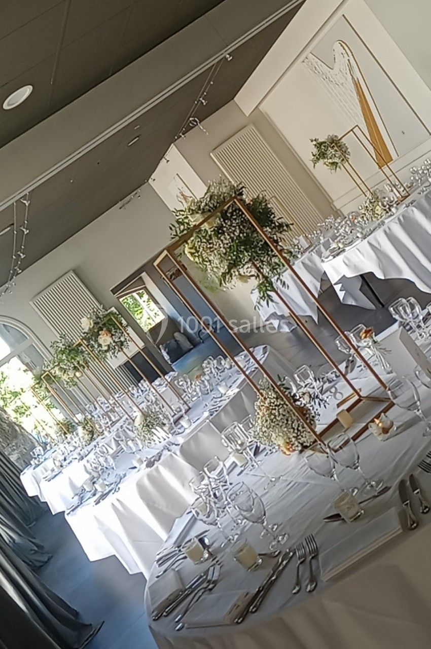Salle de réception décorée avec des tables dressées, nappes blanches et centres de table fleuris sur structures dorées.