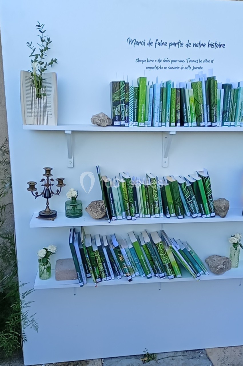 Étagères blanches décorées de livres verts, bougeoir, pierres et fleurs, installées devant un mur en pierre.