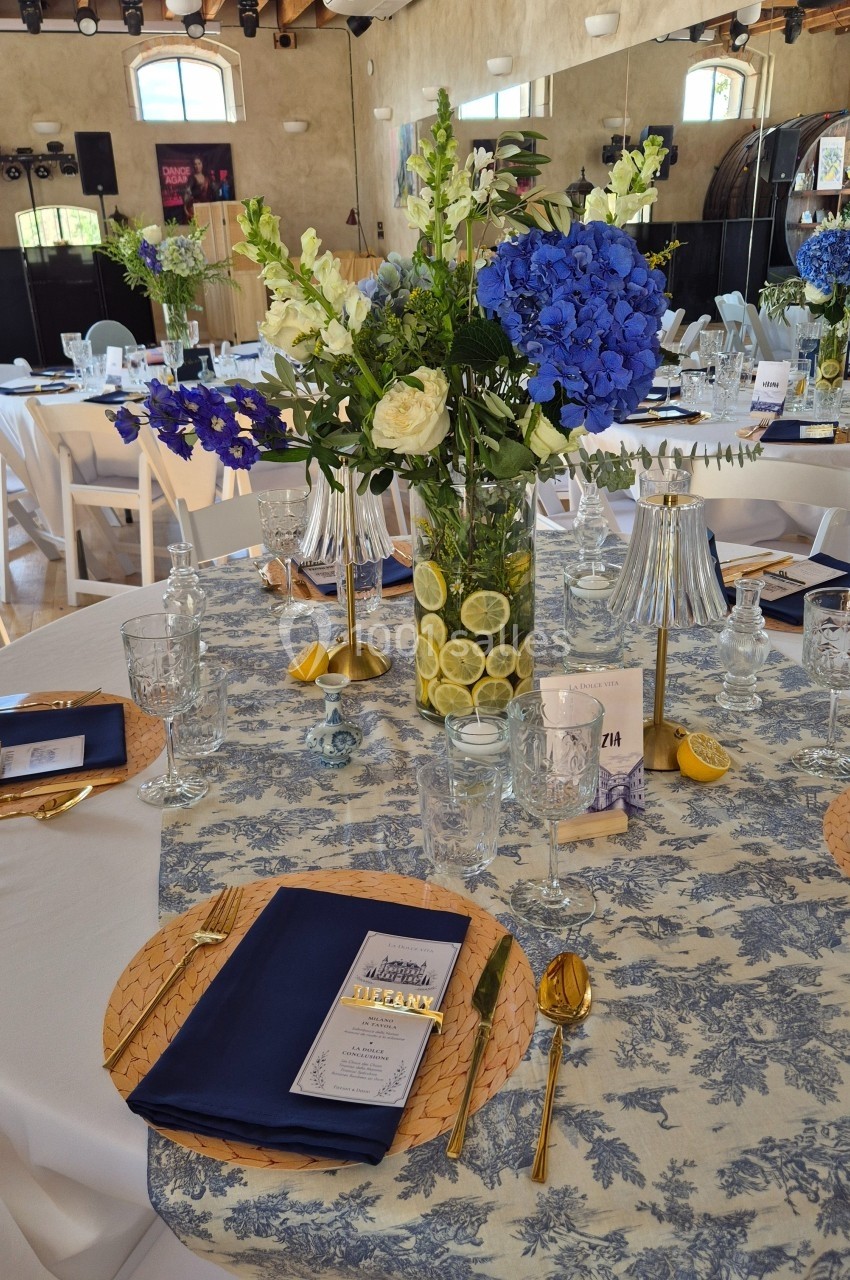 Table décorée pour un événement avec nappes fleuries, fleurs bleues et blanches, et vase rempli de rondelles de citron.