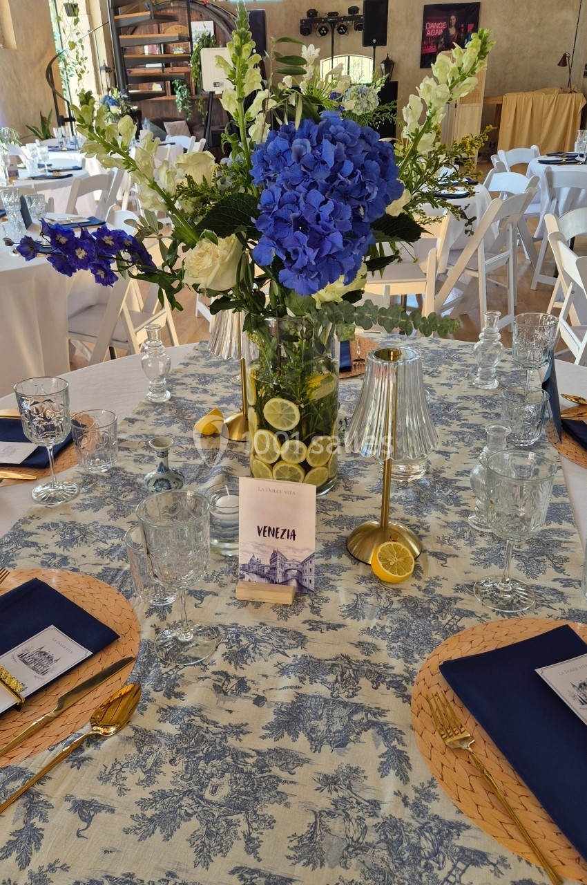 Centre de table fleuri avec hortensias bleus, citrons tranchés dans un vase, sur une nappe à motifs bleus et blancs.