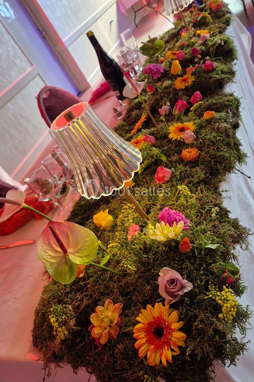 Centre de table en mousse décoré de fleurs colorées et de petites lampes, disposé sur une table de réception.