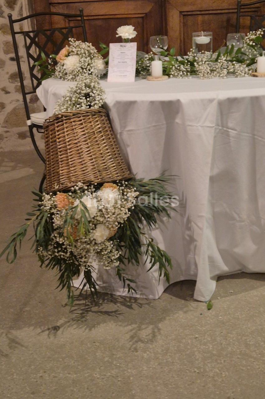 Décoration de table avec panier en osier, fleurs blanches et feuillage, disposée dans une salle au sol en pierre.