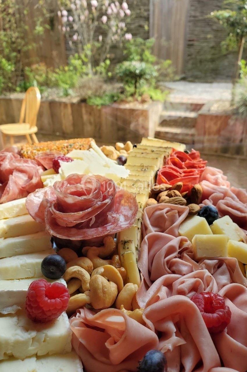 Plateau de charcuterie et fromages variés avec fruits, noix et décorations, présenté sur une table en extérieur.
