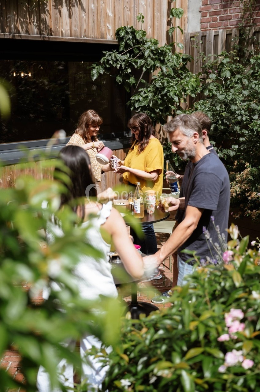 Des personnes discutent et préparent des boissons autour d'une table dans un jardin verdoyant.