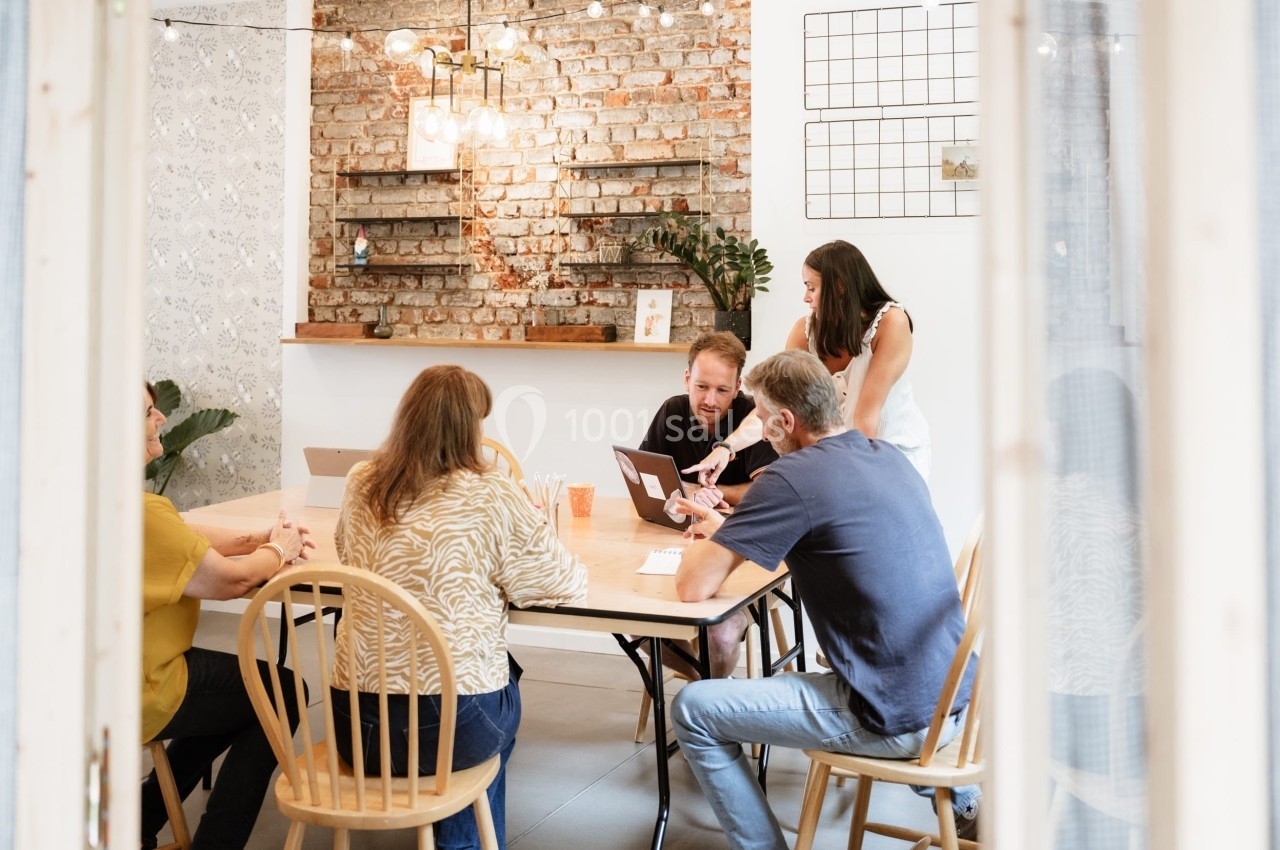 Un groupe de personnes discute autour d'une table dans une salle lumineuse avec un mur en briques apparentes.