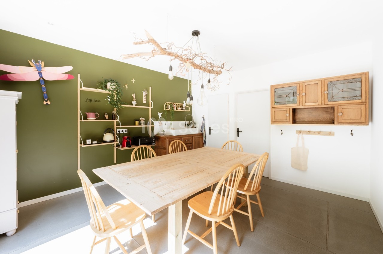 Salle à manger lumineuse avec table en bois, chaises assorties, étagères vertes et décoration murale naturelle.