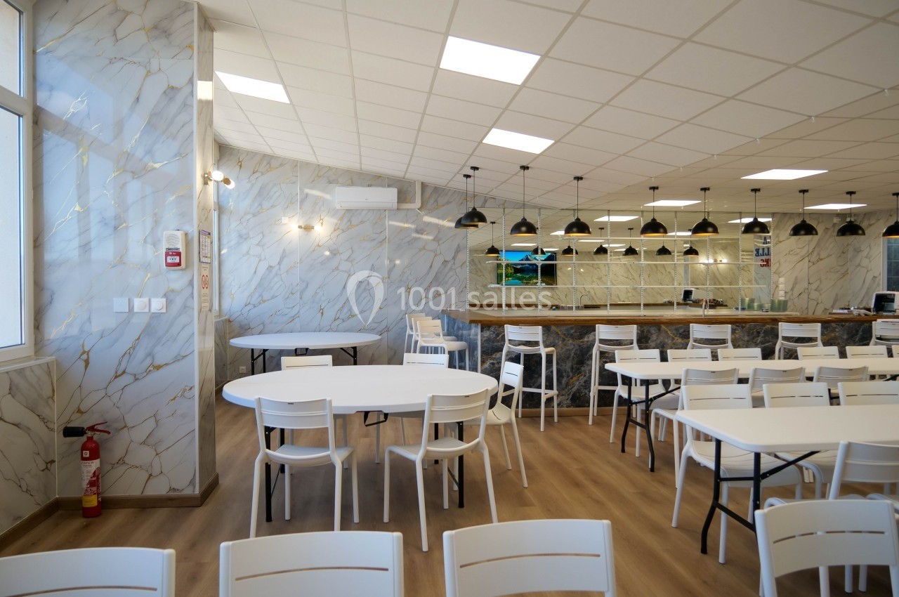 Salle de restauration lumineuse avec tables et chaises blanches, murs effet marbre et comptoir en arrière-plan.
