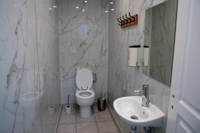 Salle de bain moderne avec lavabo, miroir rond, toilettes et urinoir, murs en marbre et sol carrelé.