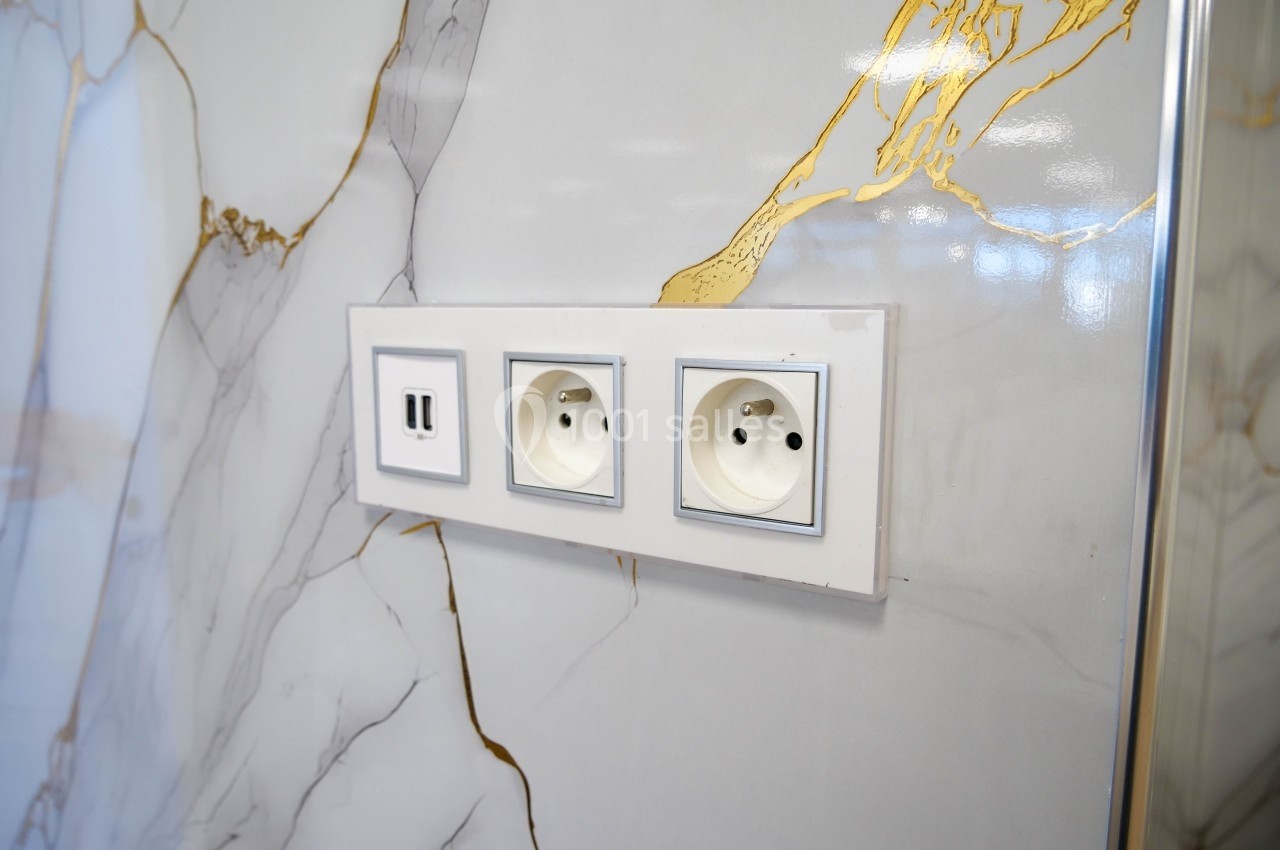 Prise électrique double et port USB intégrés dans un mur au revêtement effet marbre avec des veines dorées.