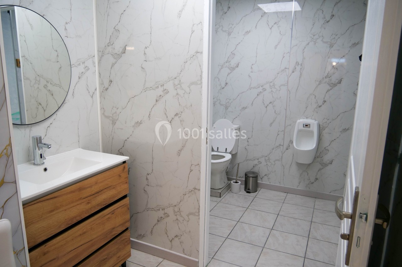 Salle de bain moderne avec lavabo, miroir rond, toilettes et urinoir, murs en marbre et sol carrelé.