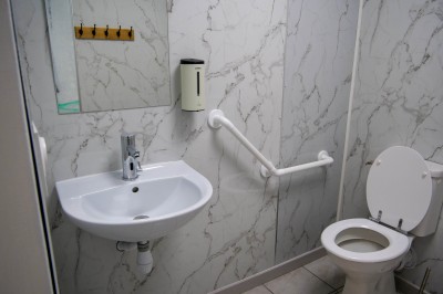 Salle de bain moderne avec lavabo, miroir rond, toilettes et urinoir, murs en marbre et sol carrelé.