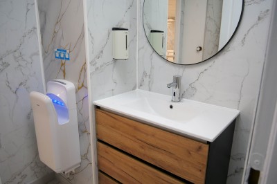 Salle de bain moderne avec lavabo, miroir rond, toilettes et urinoir, murs en marbre et sol carrelé.