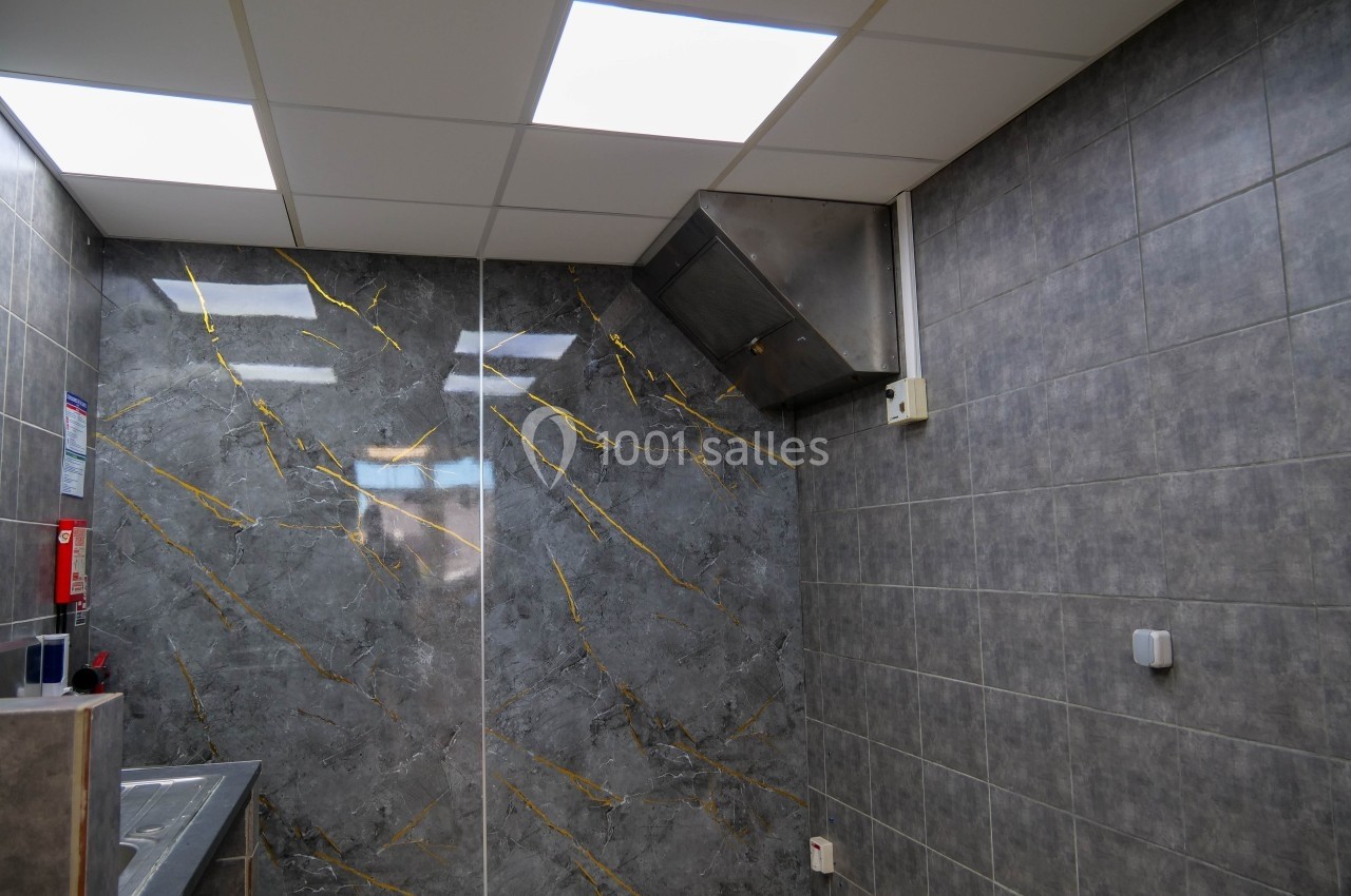 Mur en carrelage gris avec veines dorées dans une pièce équipée de plafonniers et d'une hotte murale.