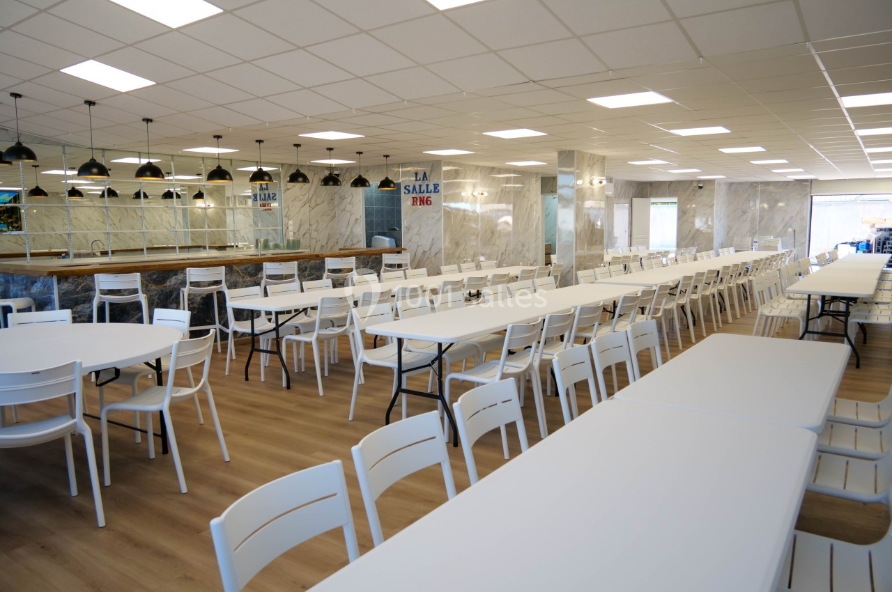 Salle de restauration spacieuse avec des tables blanches alignées et des chaises assorties sous un éclairage suspendu.