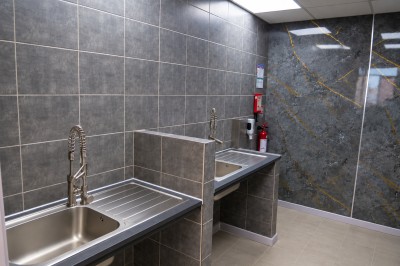 Salle de bain moderne avec lavabo, miroir rond, toilettes et urinoir, murs en marbre et sol carrelé.
