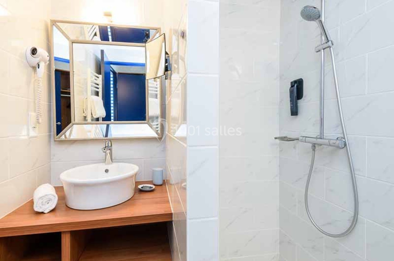 Salle de bain moderne avec lavabo à poser sur un meuble en bois, miroir encadré, sèche-cheveux mural et douche à l'italienne carrelée de blanc. Wait, "douche à l'italienne" is an inference (no walls/receding floor visible clearly). Safer: "douche avec