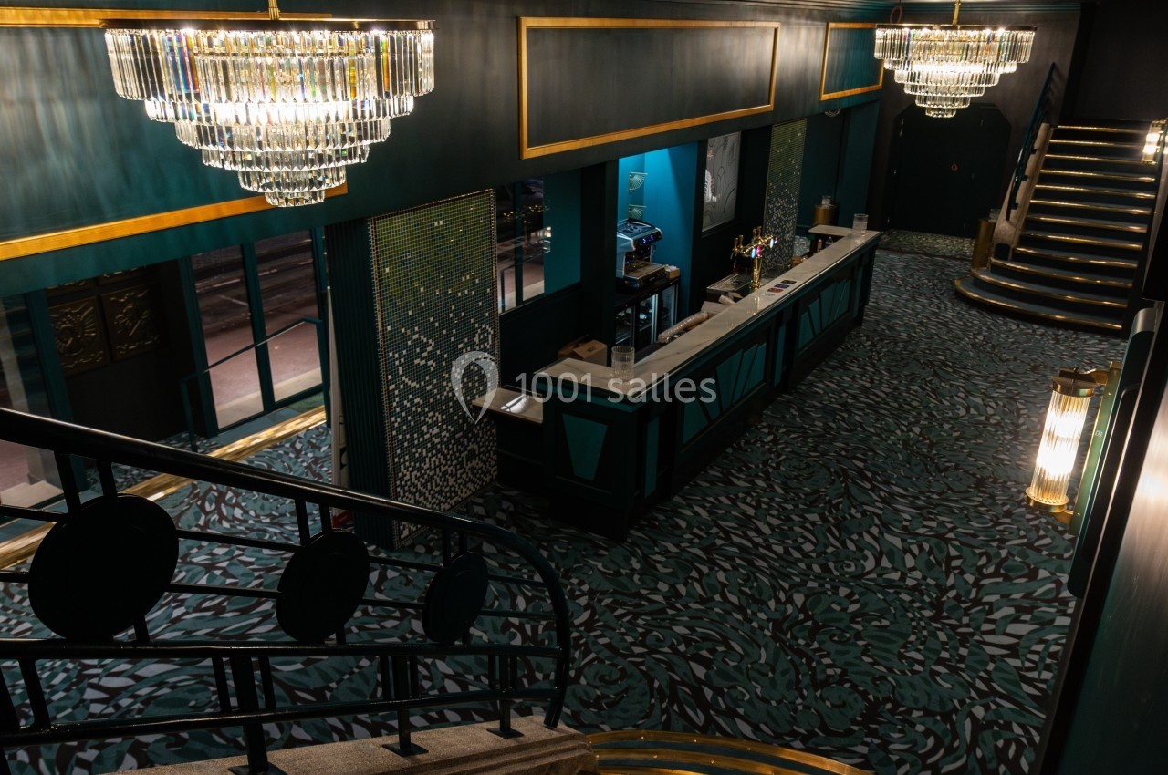 Vue intérieure d'un hall élégant avec un bar, des lustres en cristal et un escalier décoré de tapis à motifs.