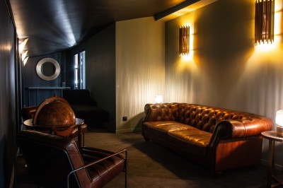 Salle de réunion avec table rectangulaire noire, chaises rouges, murs en bois strié et écran mural.