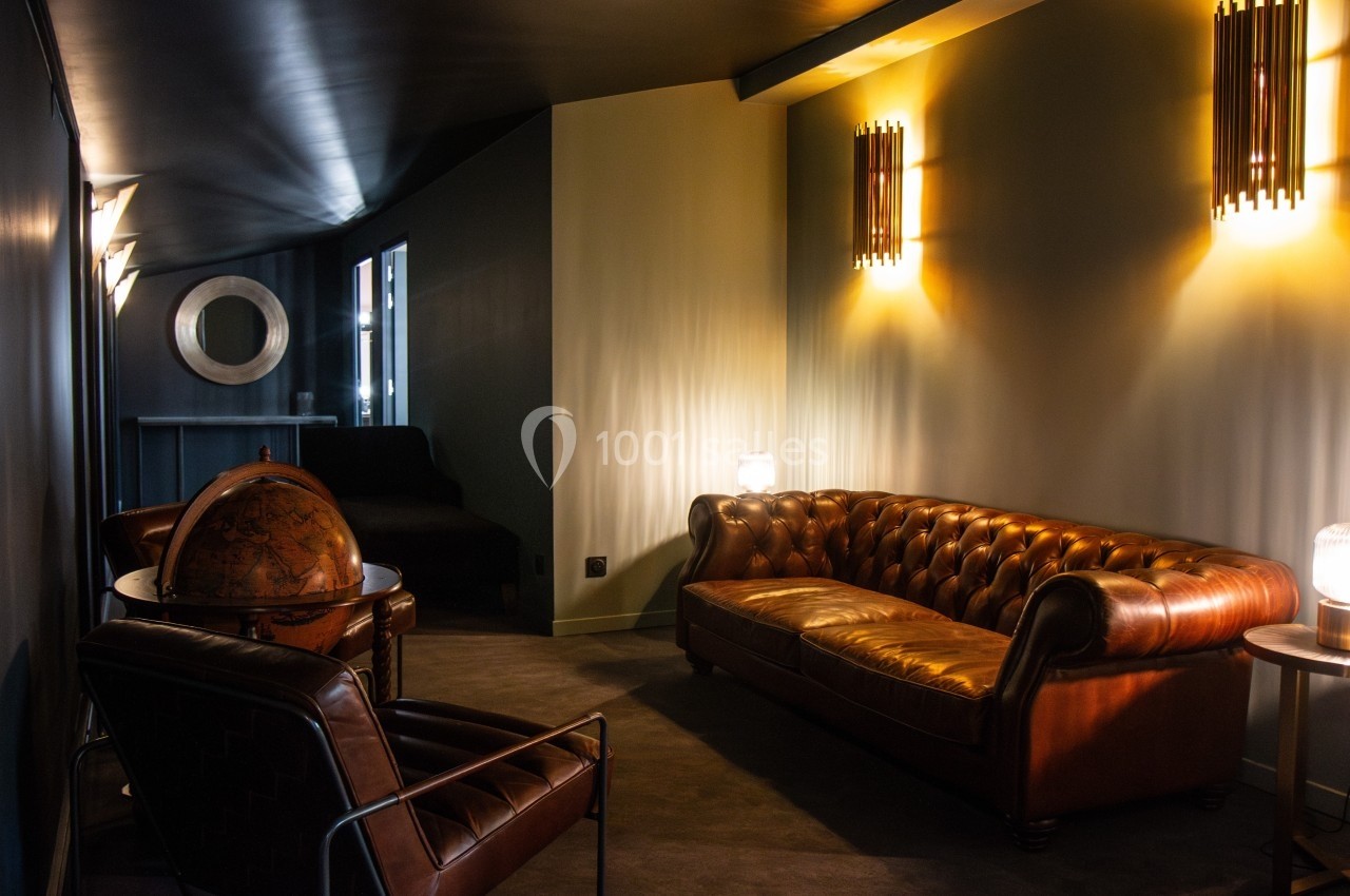 Salon cosy avec canapé en cuir marron, fauteuils assortis, globe terrestre et éclairage tamisé.