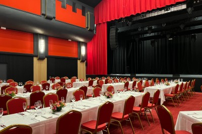 Miniature La Grande Salle - Format banquet Salle de réunion avec table rectangulaire noire, chaises rouges, murs en bois strié et écran mural.