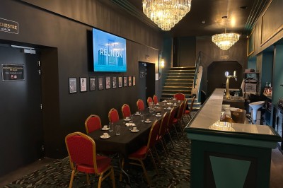 Salle de réunion avec table rectangulaire noire, chaises rouges, murs en bois strié et écran mural.
