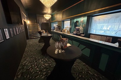 Miniature Le Hall - Espace bar en format cocktail Salle de réunion avec table rectangulaire noire, chaises rouges, murs en bois strié et écran mural.