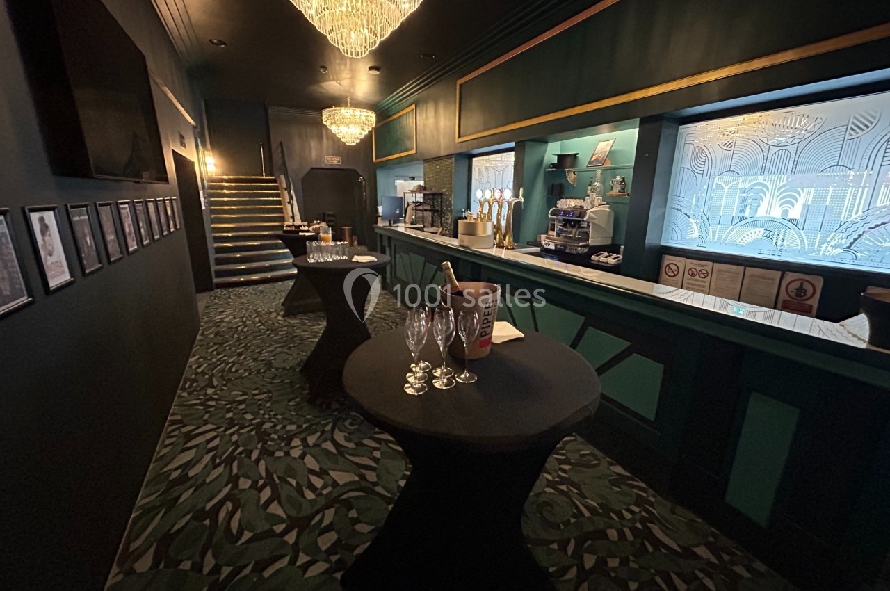 Salle élégante avec bar, tables hautes noires, seaux à champagne et lustres suspendus dans une ambiance tamisée.
