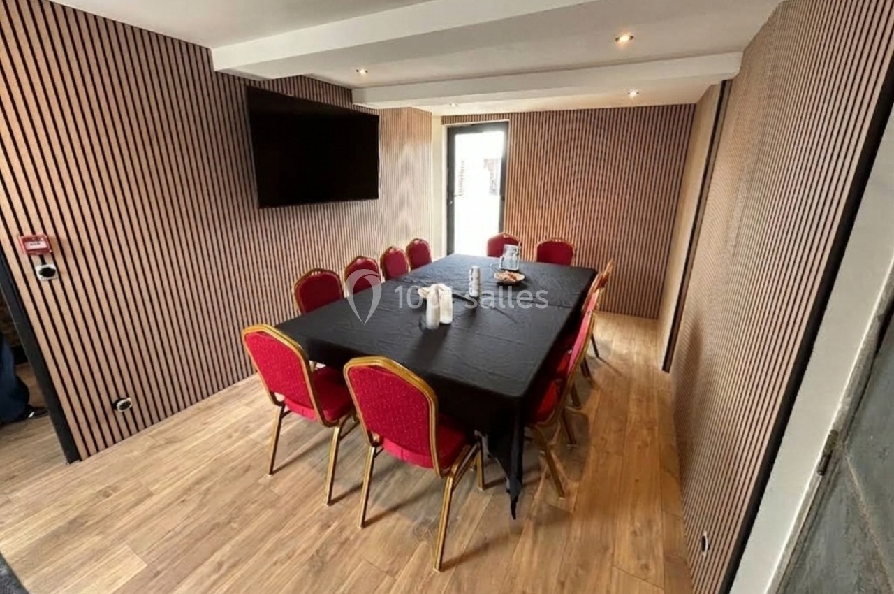 Salle de réunion avec table rectangulaire noire, chaises rouges, murs en bois strié et écran mural.