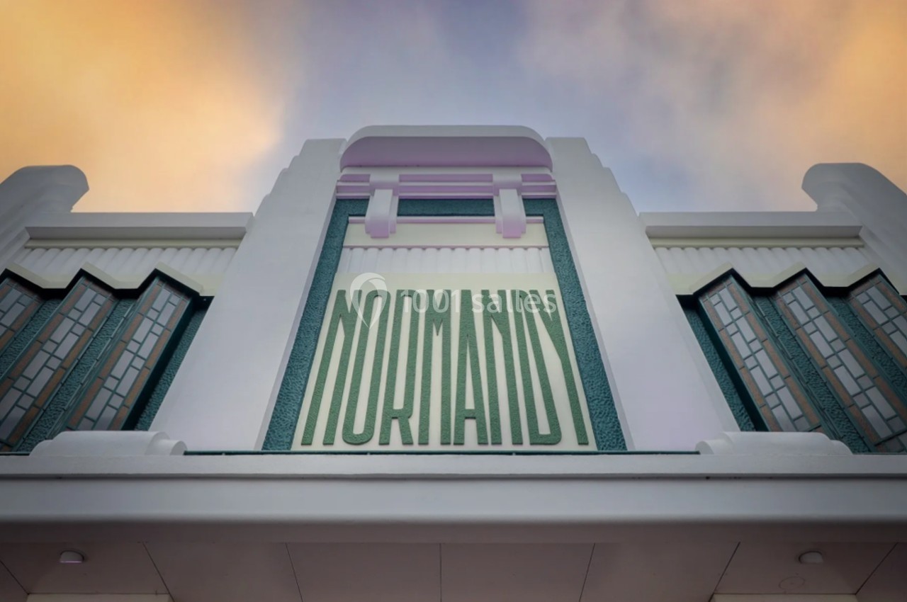 Façade art déco d'un bâtiment avec l'inscription ’Normandy’ en lettres vertes sur fond pastel.