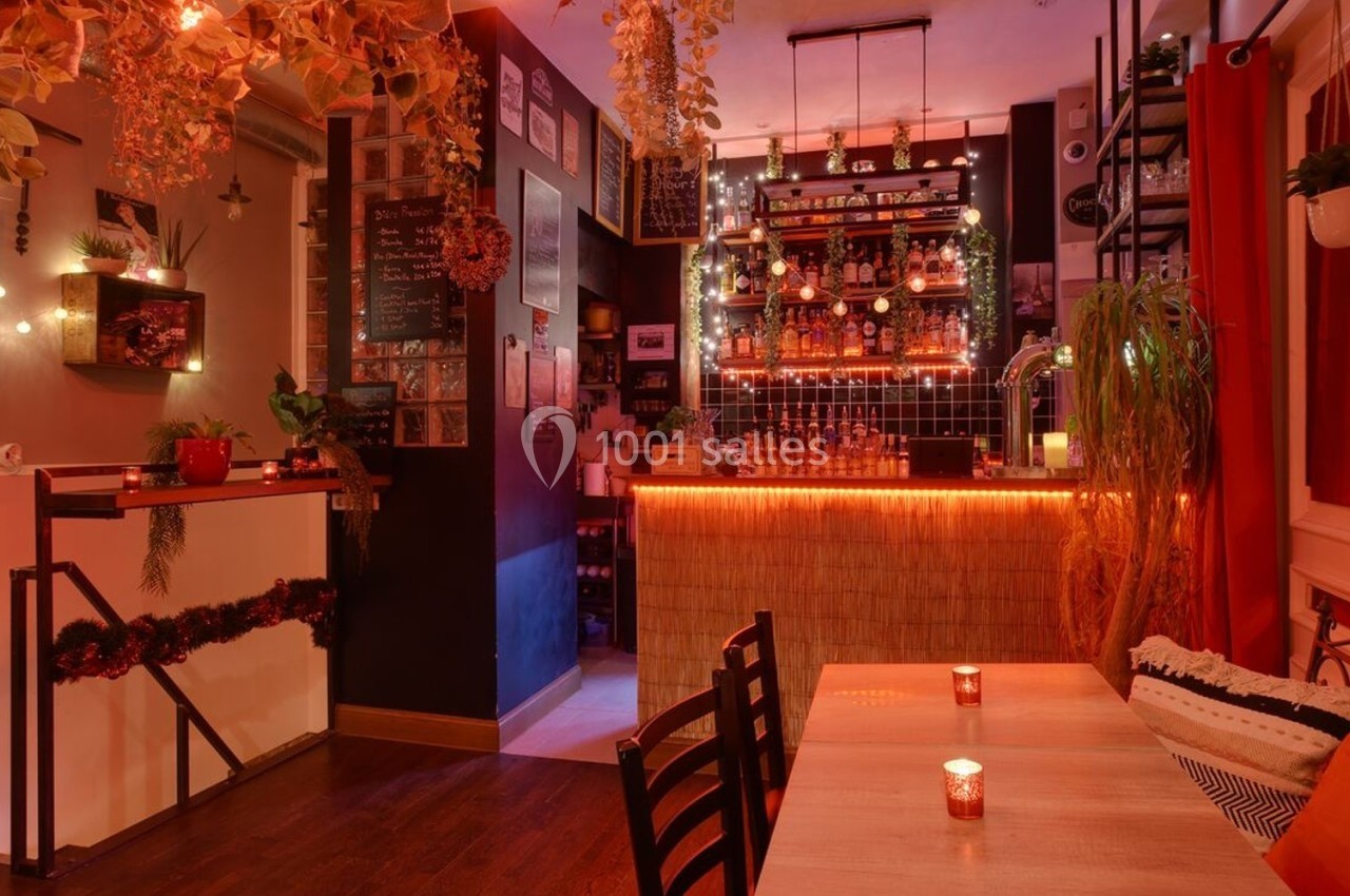 Intérieur chaleureux d'un bar avec éclairage tamisé, décorations végétales et bougies sur les tables.