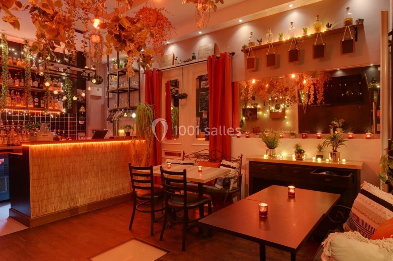Salle de restaurant chaleureuse avec éclairage tamisé, décorations végétales et bougies sur les tables.