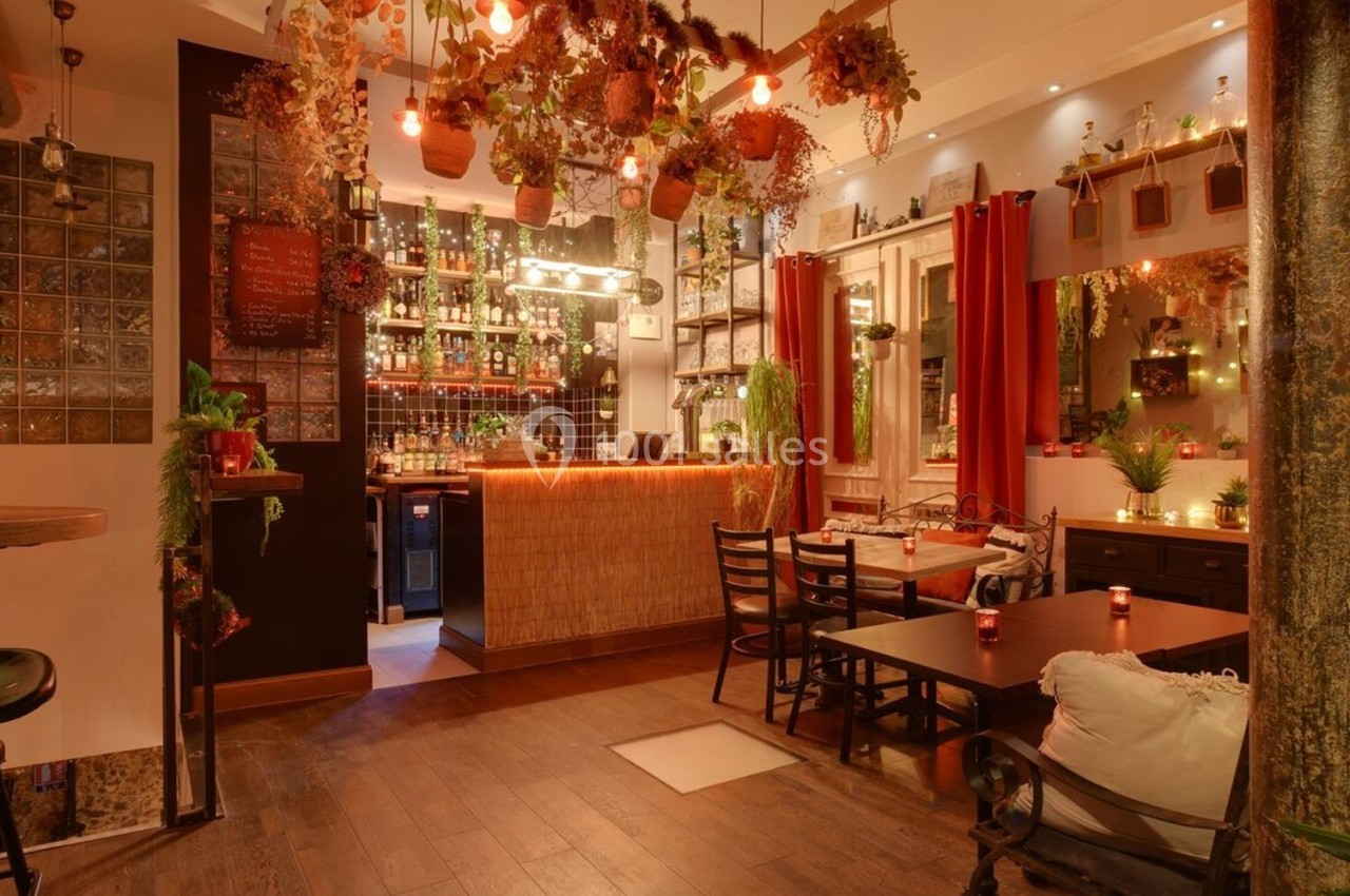 Salle de restaurant chaleureuse avec décoration végétale suspendue, éclairage tamisé et mobilier en bois.